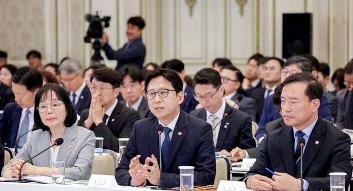 정책 브리핑 탁자에 앉은 정부 부처 장관들, 한 사람이 발언하는 동안 다른 이들이 경청하고 있다