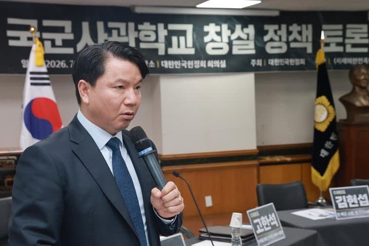 Deputy Defense Minister Kim Hong-cheol speaking into a microphone at a policy forum, with Korean flags and a banner behind him