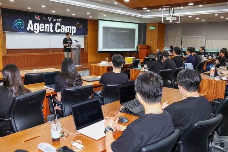 KT employees seated with laptops in a conference room facing a stage with a screen reading kt times Palantir Agent Camp
