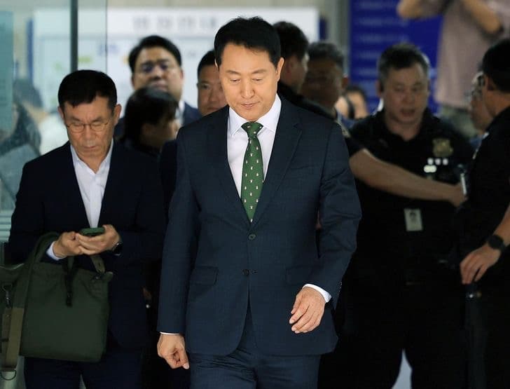 Seoul Mayor Oh Se-hoon in a dark suit and green tie walking through a courthouse corridor amid aides and security
