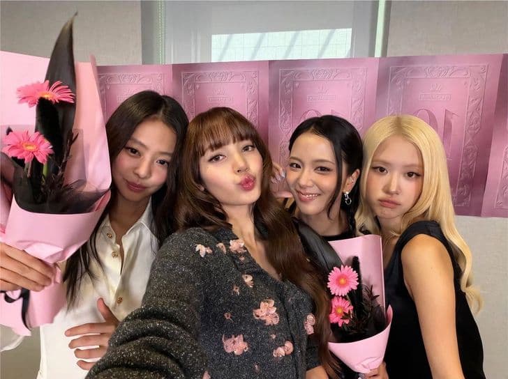 The four members of BLACKPINK pose for a selfie holding pink bouquets.