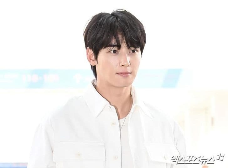 Singer and actor Cha Eun-woo, dressed in a white shirt, looks toward the camera at an airport.