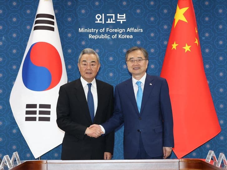 South Korean Foreign Minister Cho Hyun and Chinese Foreign Minister Wang Yi shake hands in front of the South Korean and Chinese flags.