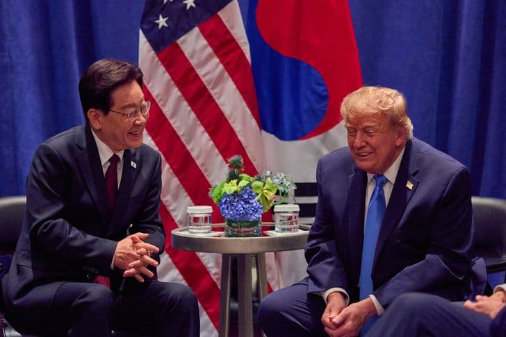 President Lee Jae-myung and President Trump sit talking together in front of South Korean and US flags.