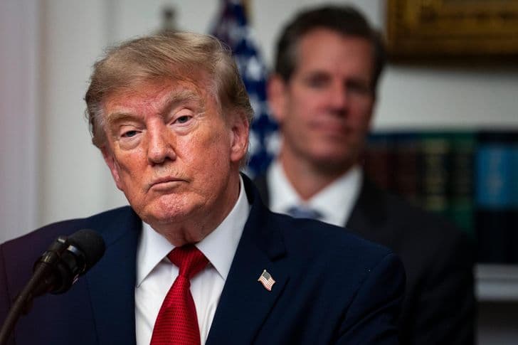 President Trump speaks at a lectern in the White House with an aide standing behind him.