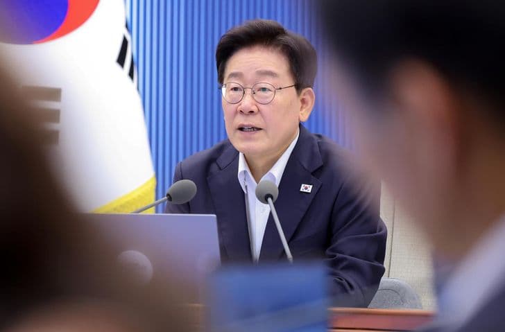 President Lee Jae-myung speaks into a microphone at a meeting with the national flag behind him.