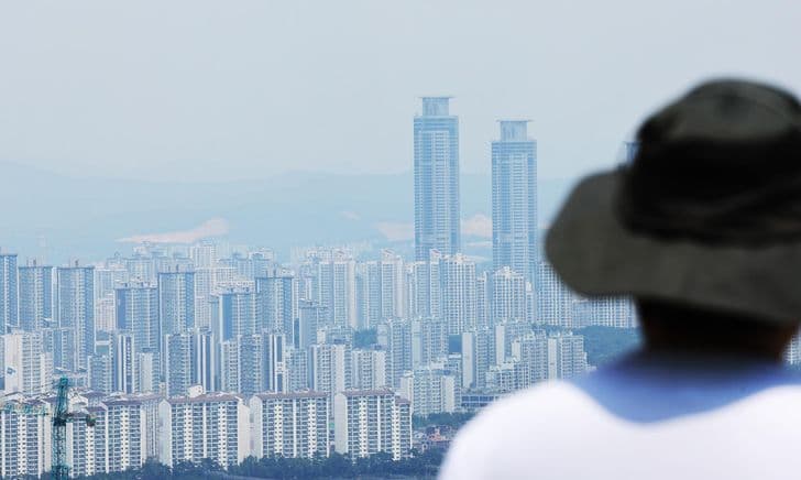 A man in a bucket hat looks out over a dense skyline of high-rise apartments in Gyeonggi Province.