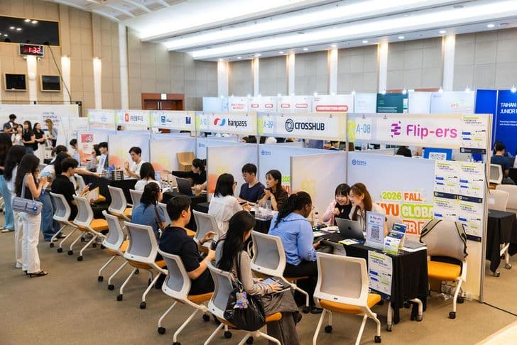 Students and company representatives sit across from each other at booths inside a crowded career fair hall.