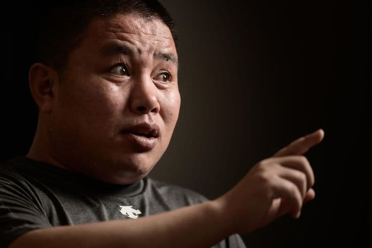 A man points and speaks in front of a dark background.