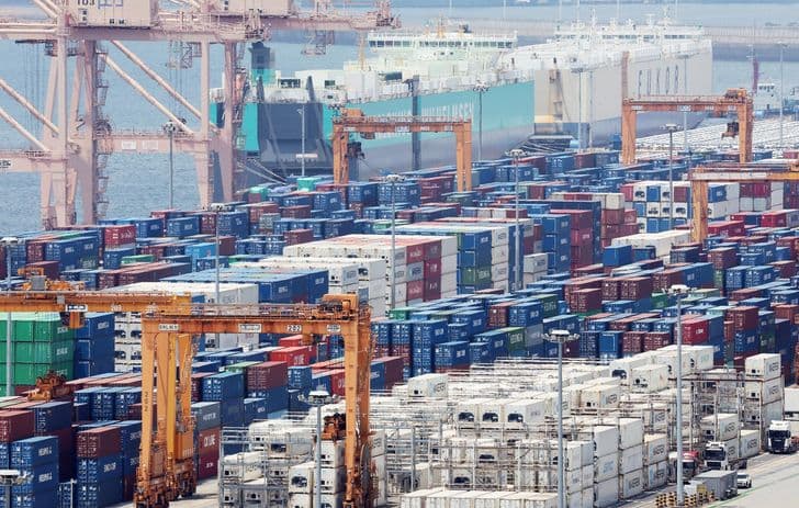 Stacked shipping containers and cargo cranes at a South Korean port terminal.