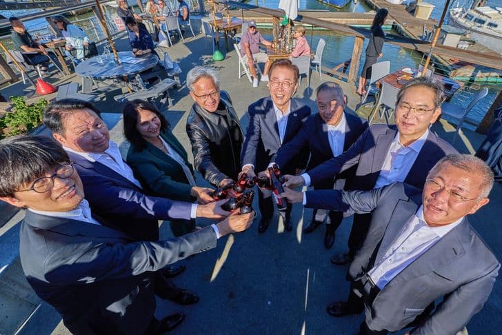 Korean and global tech executives clasp hands together over a small robot at a waterside gathering in San Francisco.