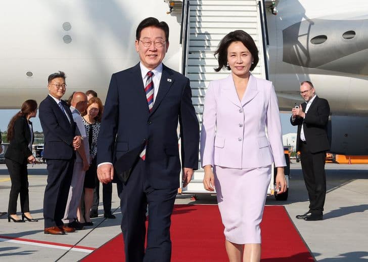 President Lee Jae-myung and his spouse walk down the aircraft stairs onto a red carpet on returning to Korea.