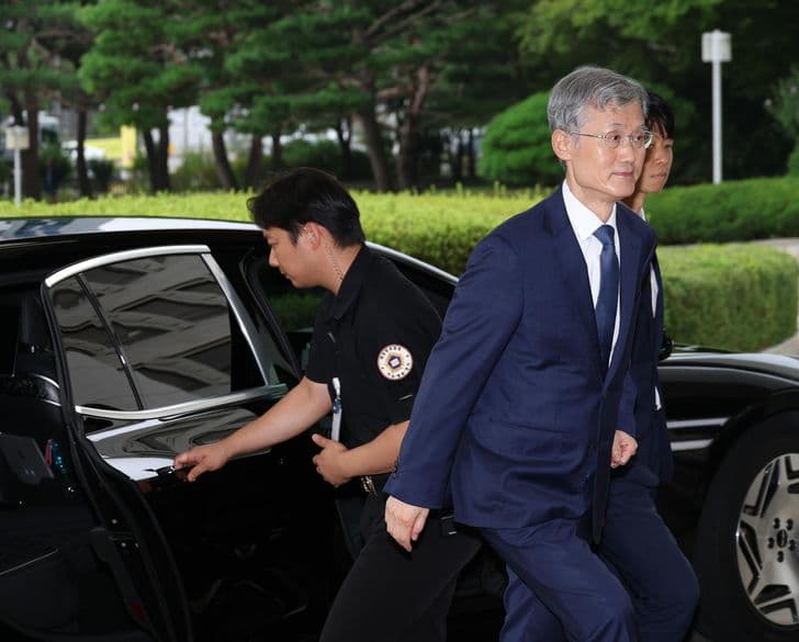 A man in a suit walks briskly away from a car with an escort behind him outside a courthouse.