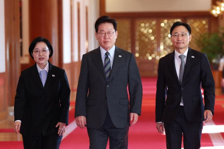 이재명 대통령이 대통령실 레드카펫 위에서 관계자 두 명과 함께 걷고 있다.