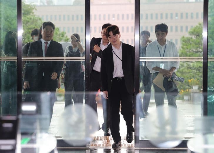 A man walks through the glass entrance of a government building as officials look on.