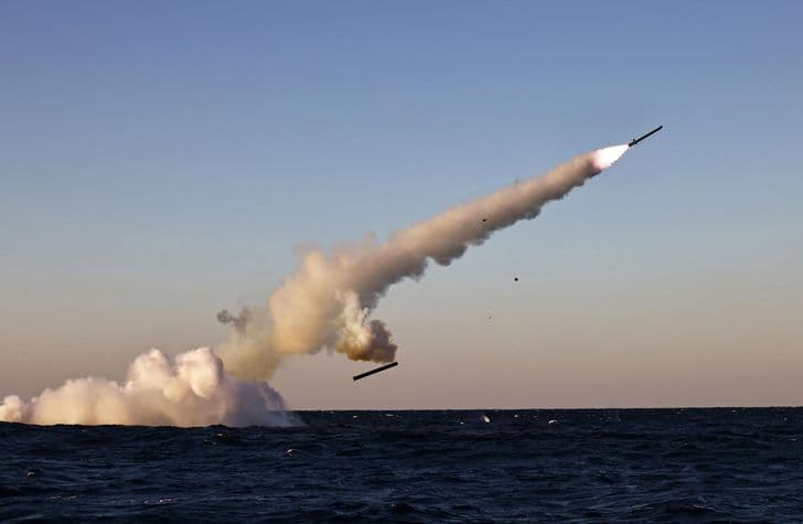 A torpedo-like weapon launches from underwater, trailing smoke and spray above the sea.