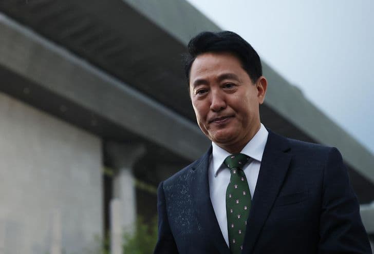 Seoul Mayor Oh Se-hoon stands outdoors in a dark suit and green tie.