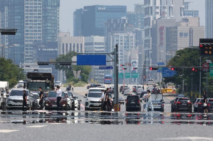 Heat haze shimmers over a Seoul road as cars and pedestrians cross under a blazing sun.