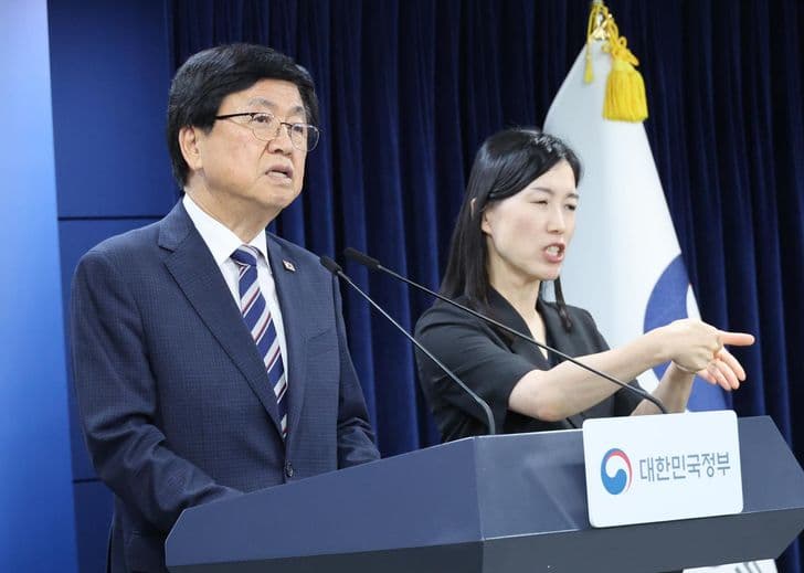 Education Minister Choi Kyo-jin speaks at a podium as a female official gestures beside him during a briefing.