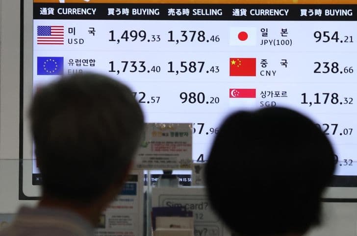 Two people look at a currency exchange board displaying dollar, euro, yen and yuan rates at a booth in Korea.
