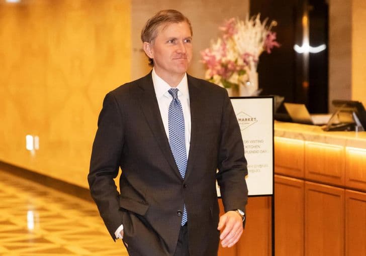 A man in a dark suit walks through a hotel lobby.